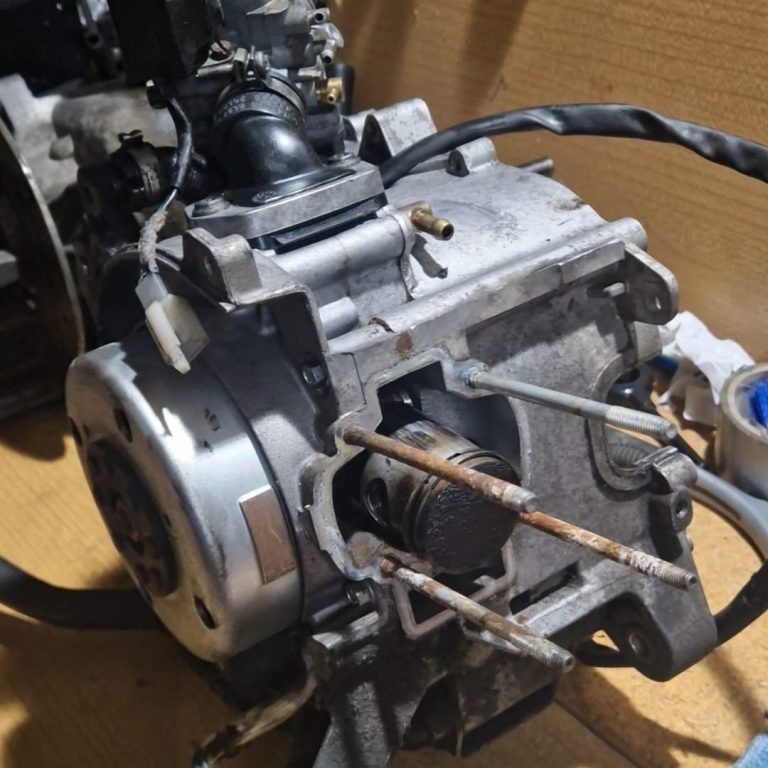 Ein Motorradmotor mit Zylinderkopf und Anschlussleitungen auf einem Karton.