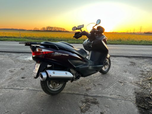 Schwarzer Roller vor einem Sonnenuntergang mit Feld im Hintergrund.