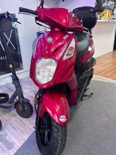 Roter Scooter mit schwarzem Sitz, steht auf einem grauen Teppich.