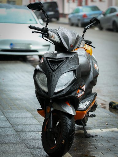 Schwarzer Motorroller mit orangefarbenen Akzenten parkt auf der Straße.