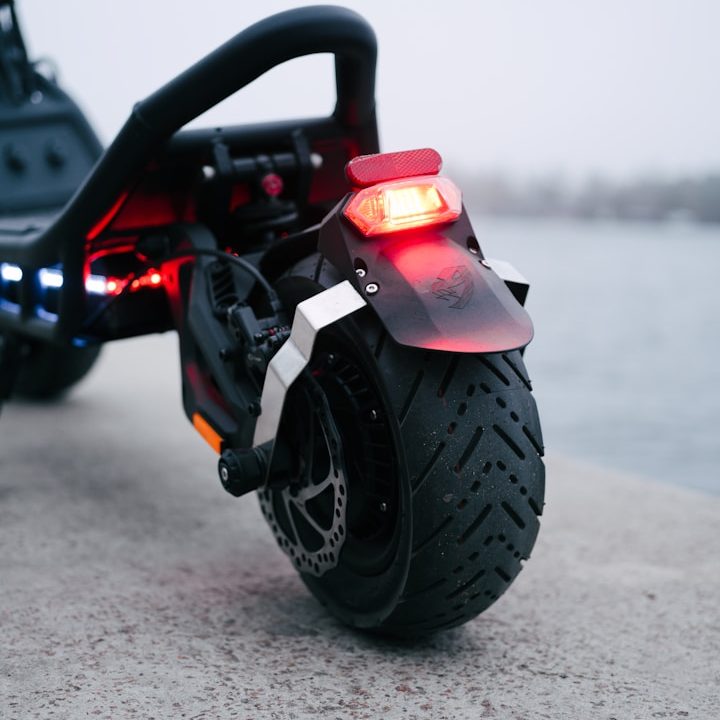 Nahaufnahme eines elektrischen Scooter-Hinterrades mit rotem Rücklicht und Reifenprofil.