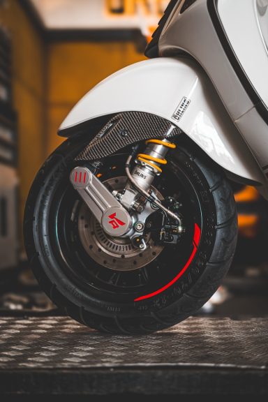 Nahaufnahme eines weißen Scooter-Reifens mit rotem Akzent und Bremsanlage.
