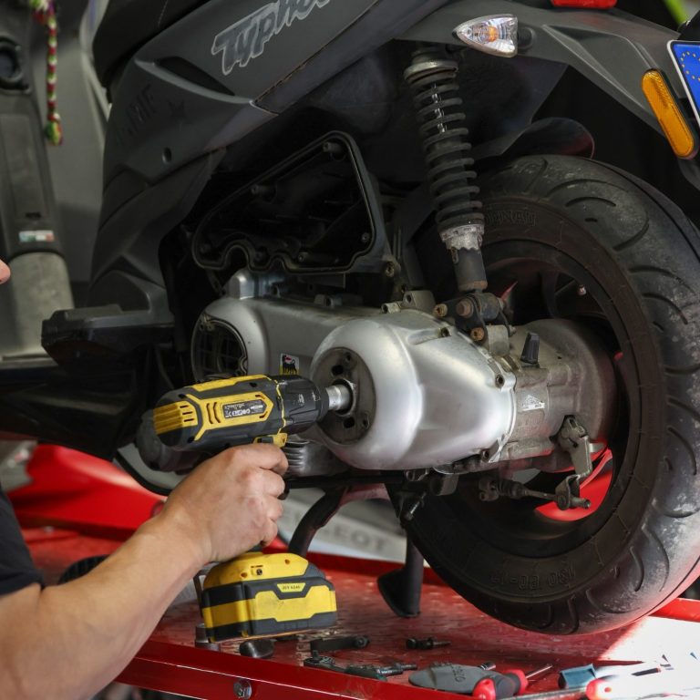 Mann schraubt an einem Motorroller in einer Garage mit Akkuschrauber