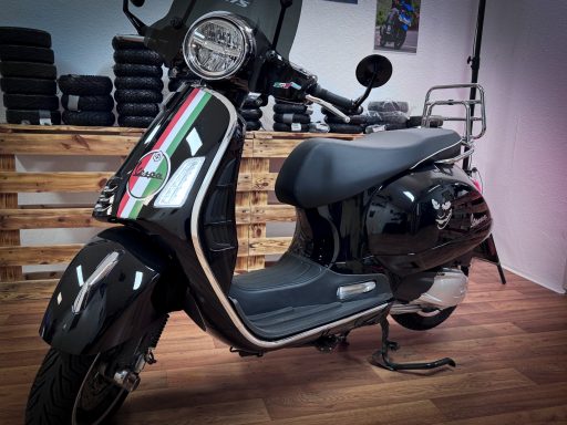 Schwarzer Scooter mit italienischen Flaggenfarben, auf einem Holzboden in einem Geschäft.